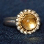 Zilveren ring met citriencabochon in gouden kast, parelrand